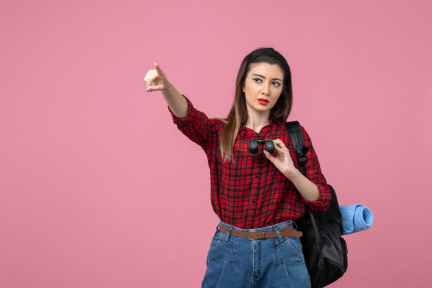 人正面图：穿着红色衬衫的年轻女性 用望远镜在粉色背景上观察人类女性人年轻女性头发