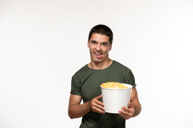 电影正面图身穿绿色t恤的年轻男性手持土豆cips在浅白的墙上看电影人孤独的电影咖啡电影浅白色
