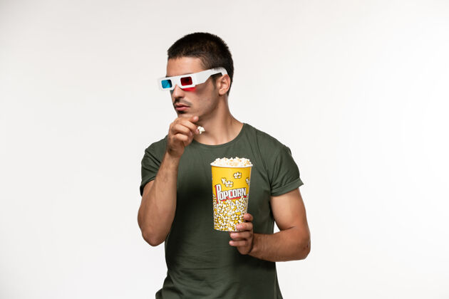 成人正面图身着绿色t恤 戴着d型太阳镜 手持爆米花的年轻男性在浅白的墙上拍摄电影《孤独电影院》男性电影电影电影爆米花