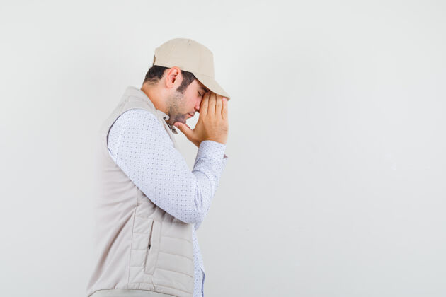 休闲年轻人穿着米色夹克 戴着帽子 站在祈祷的姿势 专注地看着前方男性思想脸