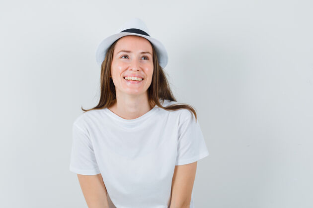 女士年轻的女士戴着白色的t恤帽子抬头望去 看上去很高兴性感人性化连衣裙