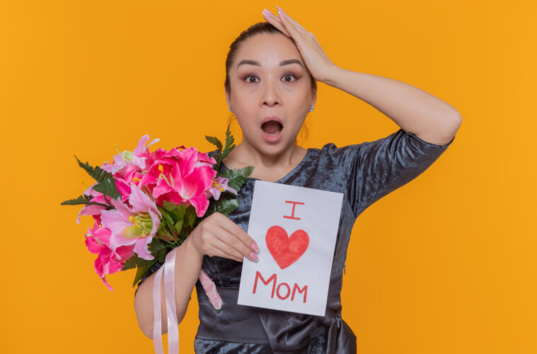 女人惊讶和惊讶的亚洲妇女母亲手持贺卡和鲜花庆祝母亲节站在橙色的墙上立场花亚洲