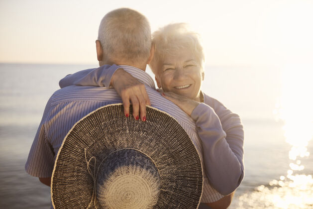 丈夫老人们在海边拥抱团聚微笑草帽