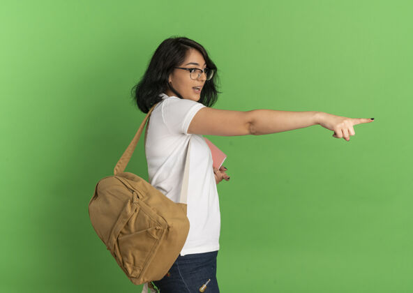 女学生年轻漂亮的白人女生 戴着眼镜 背着书包 站在一边 指着前面的绿色空间 望着前方向前侧站立