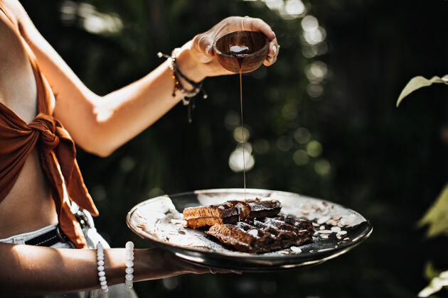 餐巾纸穿着棕色胸罩的晒黑女人拿着盛着枫糖浆的碗 在花园里摆姿势小吃黄油布鲁塞尔