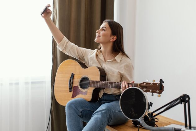 艺术家侧视图女音乐家在家里自拍 而持有原声吉他表演内部吉他