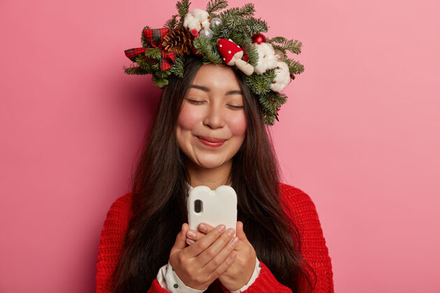 乐观头上戴着圣诞花环的年轻漂亮女人女人电话设备