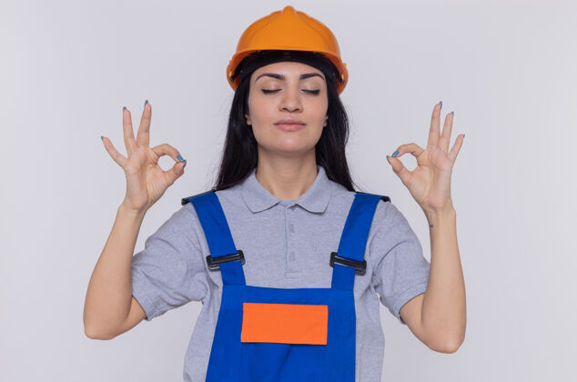 女人身穿建筑制服 头戴安全帽的年轻女建筑工人在做冥想手势建筑工安全放松