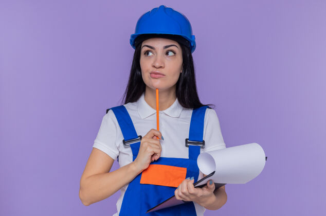 建筑年轻的建筑女工穿着建筑制服 戴着安全帽拿着剪贴板建筑工人女人站