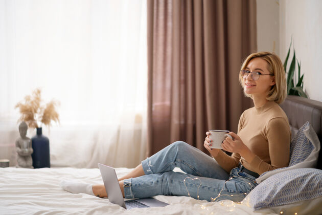 无线女人在卧室里用笔记本电脑放松 喝一杯热咖啡或茶杯子卧室自然