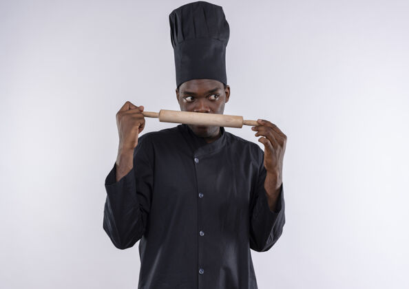 烹饪穿着厨师制服的年轻美籍黑人厨师手拿擀面杖 看着白色的一面 留着复印空间卷年轻制服