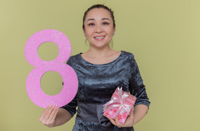 国际快乐的亚洲女人拿着纸板做的8号礼物 站在绿色的墙上 看着前面微笑着欢庆国际妇女节礼物欢呼微笑