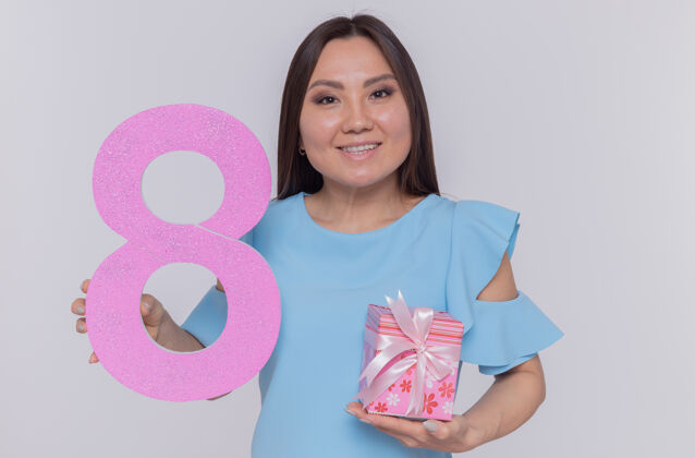 八快乐而积极的亚洲女人拿着纸板做的数字8 站在白色的墙上 看着前面微笑着欢庆国际妇女节正面站立礼物