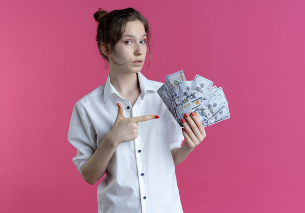 年轻年轻自信的俄罗斯金发女孩拿着粉色的钞票指着复制空间俄罗斯空间金发