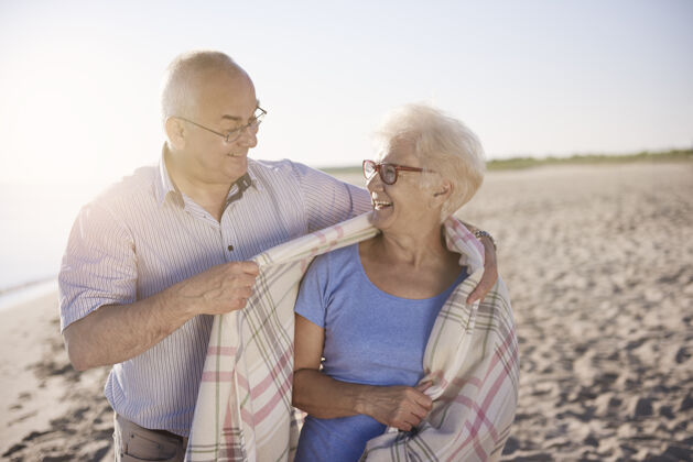 拥抱老年夫妇在沙滩 退休和暑假的概念大海毯子欢笑