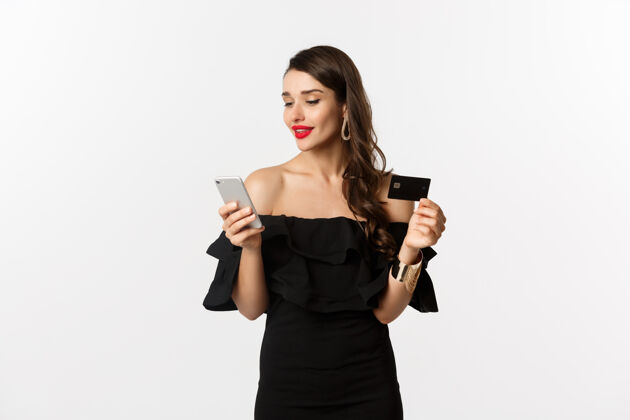 女性时尚和购物理念年轻漂亮的女人在网上购物 用信用卡和智能手机在网上购物 白色背景优雅美丽时尚