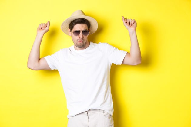 黄色旅游 旅游和度假概念男人旅游者享受假期 戴着草帽和太阳镜跳舞 在黄色背景下摆姿势男人成年人帽子