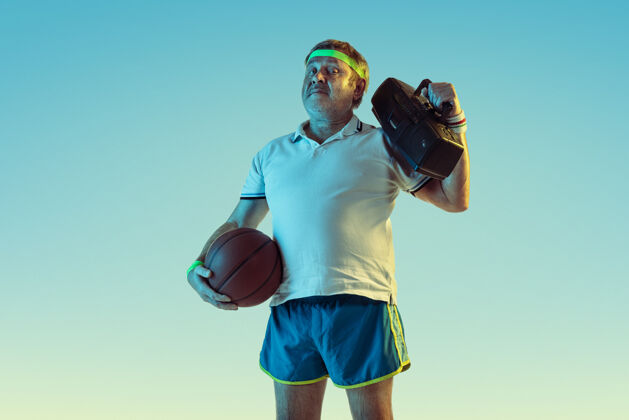 表情高级男士穿着运动装摆出令人惊艳的姿势 复古录音机放在斜墙上 霓虹灯高加索男模身形优美 充满运动气息运动的概念 活动 运动 健康的生活方式网球装备姿势