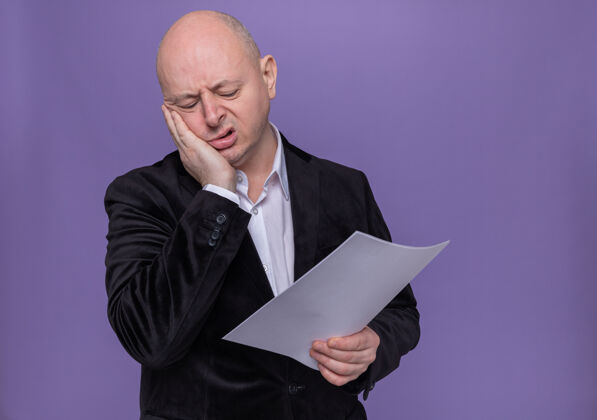 西装穿着西装的中年秃头男人站在紫色的墙上 手里拿着空白的一页 看上去又累又无聊拿着疲倦空白