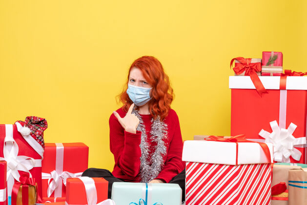 面具正面图年轻女子围坐在圣诞礼物与面具上的黄色病毒情感冠状病毒-新年的颜色前面房子笔记本电脑