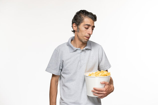 前面正面图年轻男性一边吃薯片一边在白色的表面看电影电影院偏远孤独