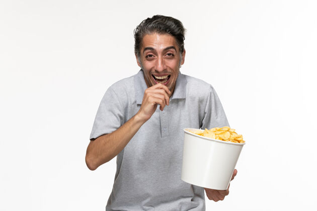 办公室正面图：年轻的男性在白色的表面上笑着吃薯片土豆笔记本电脑孤独