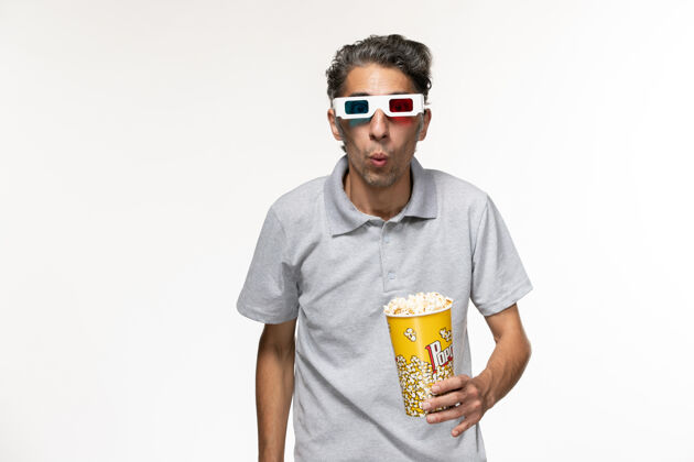 孤独正面图年轻男性手持爆米花包 戴着d型太阳镜 白色表面护目镜遥控正面