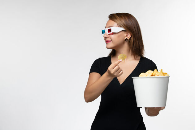 孤独正面图：年轻女性戴着d型太阳镜拿着薯片 坐在白色桌子上看电影抱着土豆书桌