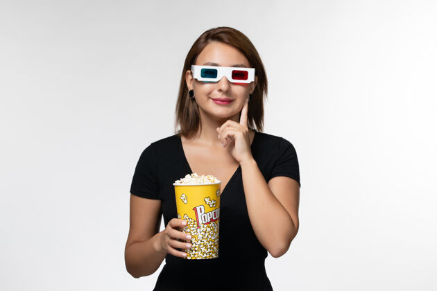 电影院正面图戴着d型太阳镜拿着爆米花的年轻女性在浅白的表面上看电影爆米花年轻女性孤独