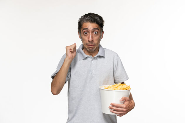 远程前视图年轻的男性吃薯片看电影在一个浅白色的表面前面孤独员工