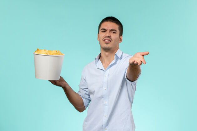 土豆正面图：浅蓝色表面上 年轻的男性拿着土豆片的篮子远程电影院男