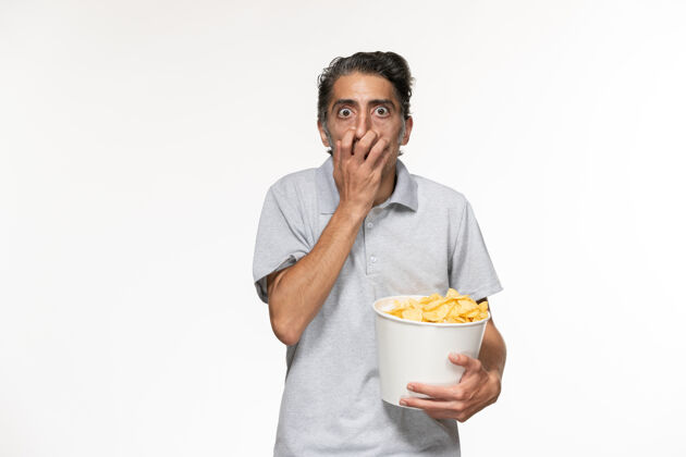 年轻的男正面图：年轻的男性拿着薯片 在白色的桌子上看电影土豆看电影院