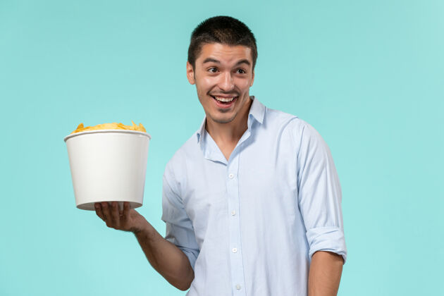 电影院正面图：年轻男性拿着蓝桌子上放着薯片的篮子杯子篮子遥控
