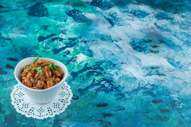 碗一碗烤豆放在杯垫上 蓝色背景美味烘焙风味