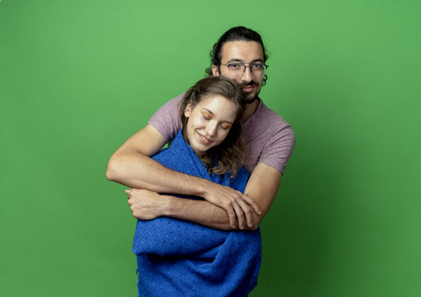 男人一对年轻的男女 热恋中的快乐 汉森的男人抱着他心爱的女朋友站在绿色的墙上毯子拥抱站着