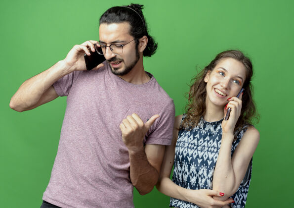 情侣一对年轻的男女 站在绿色的墙上 愉快而积极地用手机交谈站着女人积极