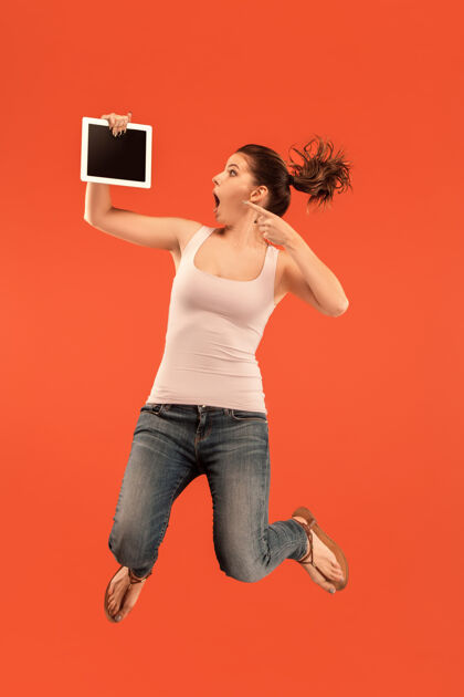 绿色年轻女子在蓝色工作室背景上跳跃时使用笔记本电脑或平板电脑小玩意在运动或运动中奔跑的女孩微笑运动运动
