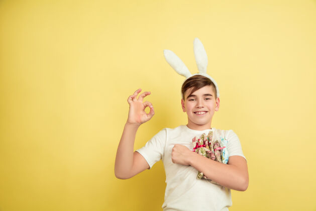 快乐男孩像复活节兔子在黄色的工作室墙上鸡蛋表情疯狂