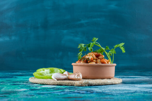 蔬菜一碗烤豆子 配欧芹 大蒜和胡椒 放在三角架上 蓝色背景碗美味胡椒