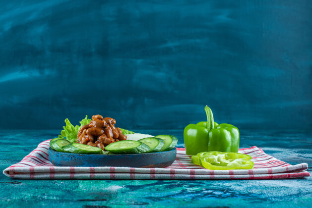 风味把切好的蔬菜和烤豆子放在毛巾上的木盘上 蓝色背景黄瓜美味毛巾