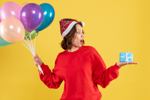颜色正面图：手持气球和小礼物的年轻女子在黄色圣诞假期新年情感色彩派对庆祝情感