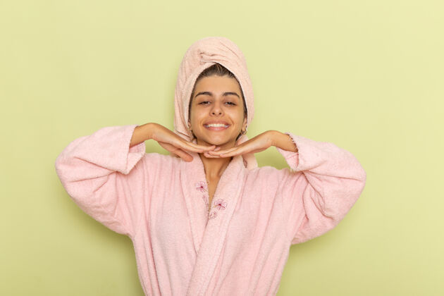 套头衫正面图穿着粉红色浴袍的年轻女性在绿色的表面上摆姿势微笑运动衫面具浴衣