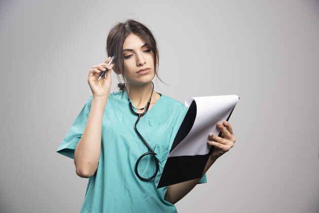 工作女医生在看剪贴板上的笔记剪贴板制服听诊器