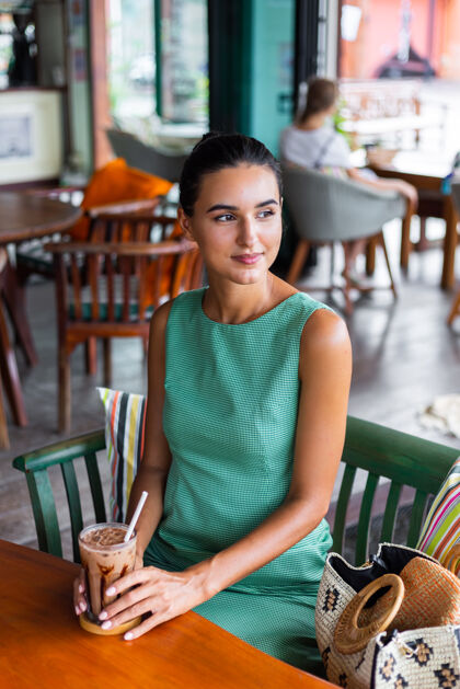 坐可爱 优雅 平静 快乐的女士 穿着绿色夏装 坐在咖啡馆里喝咖啡 享受早晨情绪一餐桌