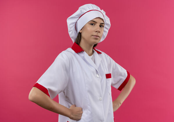 空间身着厨师制服的年轻自信的白种人厨师女孩将拳头放在腰上 看着隔离在粉色空间和复印空间的相机腰拳头厨师