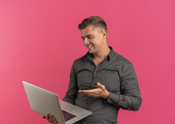 拿着年轻的金发帅哥微笑着拿着笔记本电脑 指着粉红色的空间和复印空间粉色笔记本电脑男人