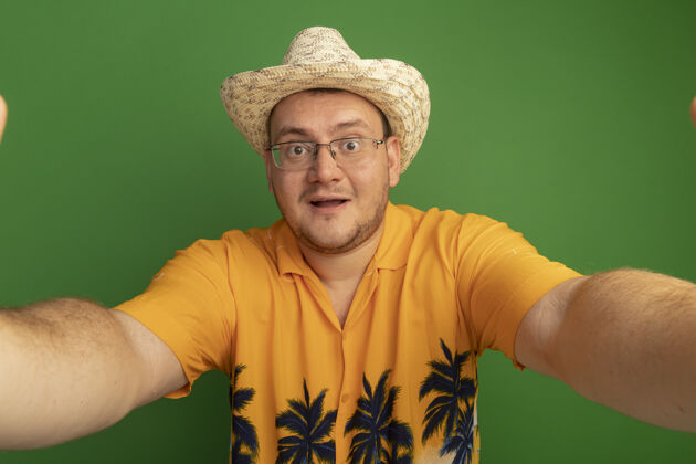 微笑戴着眼镜的男人 穿着橘色衬衫 戴着夏天的帽子 脸上带着微笑站在绿色的墙上帽子眼镜戴着