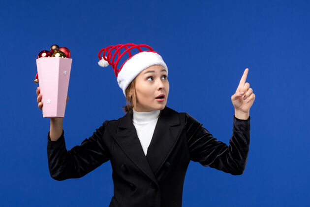 女人正面图：年轻的女性拿着树上的玩具在淡蓝色的墙上新年假期女性蓝色成功公司玩具
