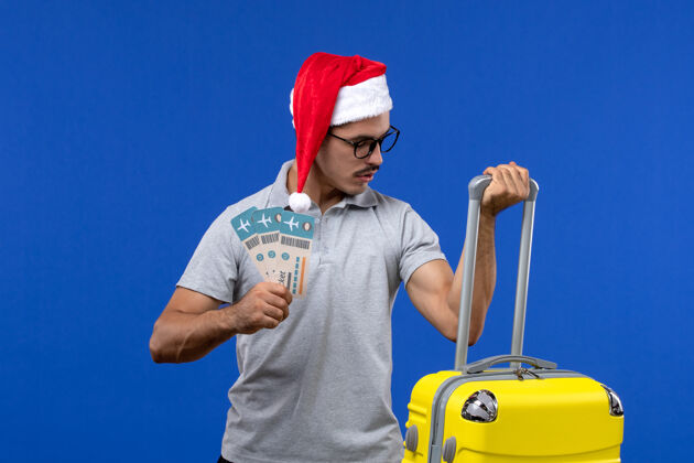 男人正面图：年轻男子提着沉重的袋子 拿着蓝墙航班度假飞机的机票携带视图工作