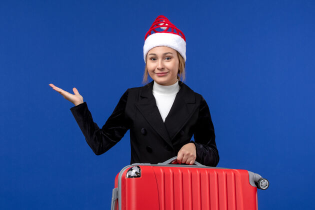 前面正面图年轻女子背着红包在蓝色的墙壁上旅行度假的女人帽子年轻女性职业